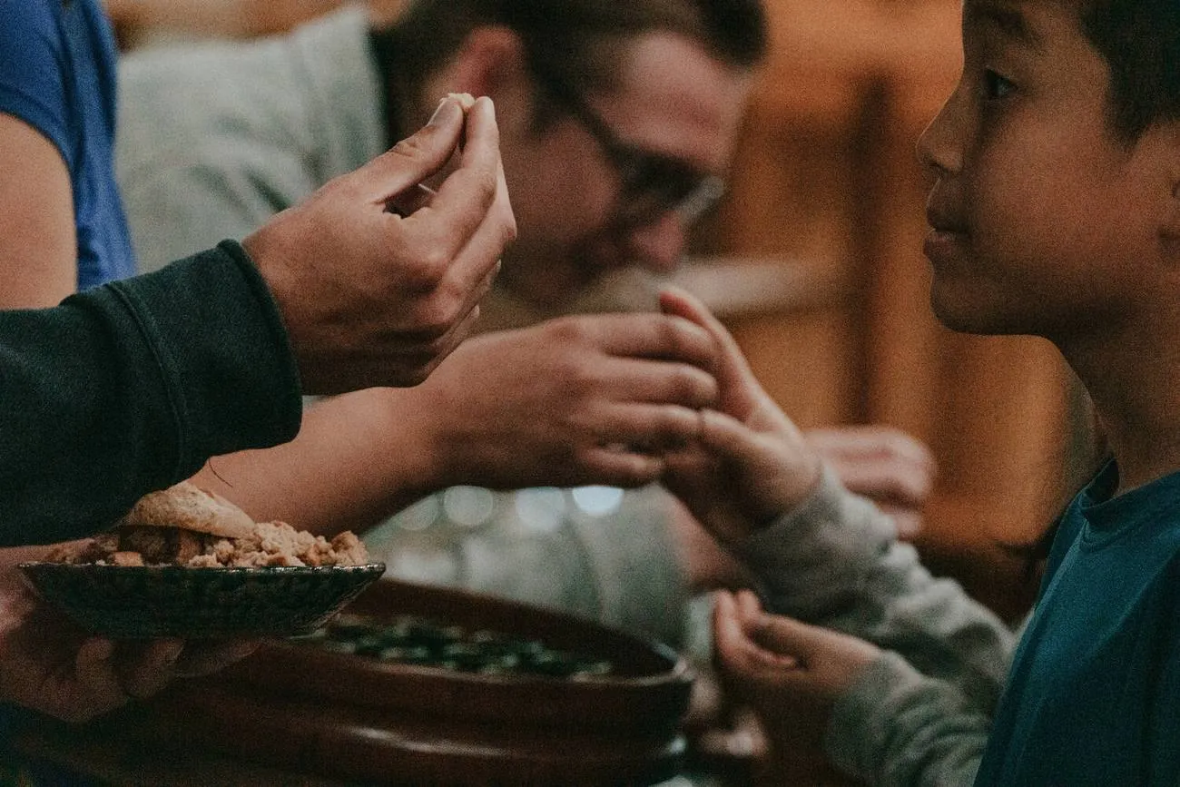 Bread broken and handed into a child's reaching hands.