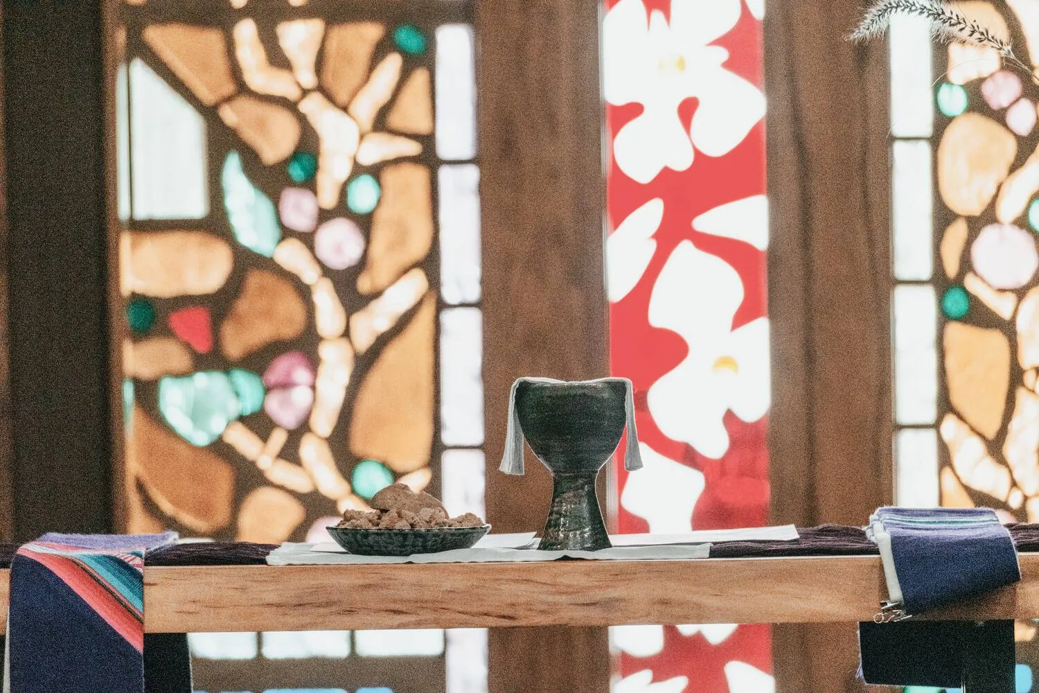 The communion table set with bread and a chalice before the stained glass.