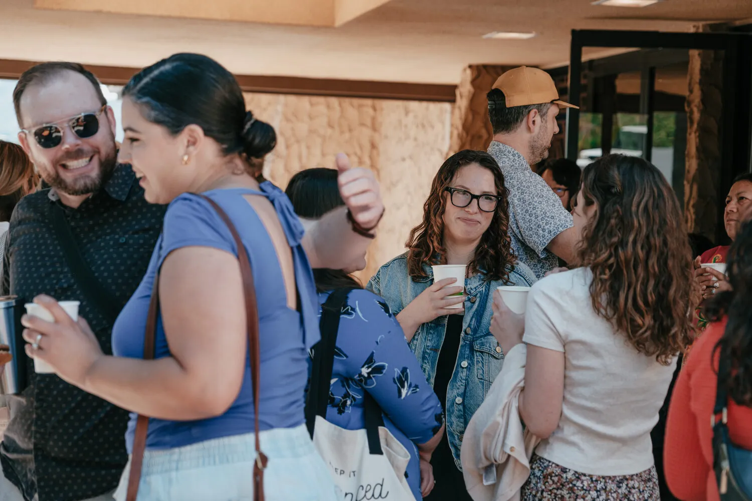 Two people laughing face to face over coffee, with the congregation talking behind them.